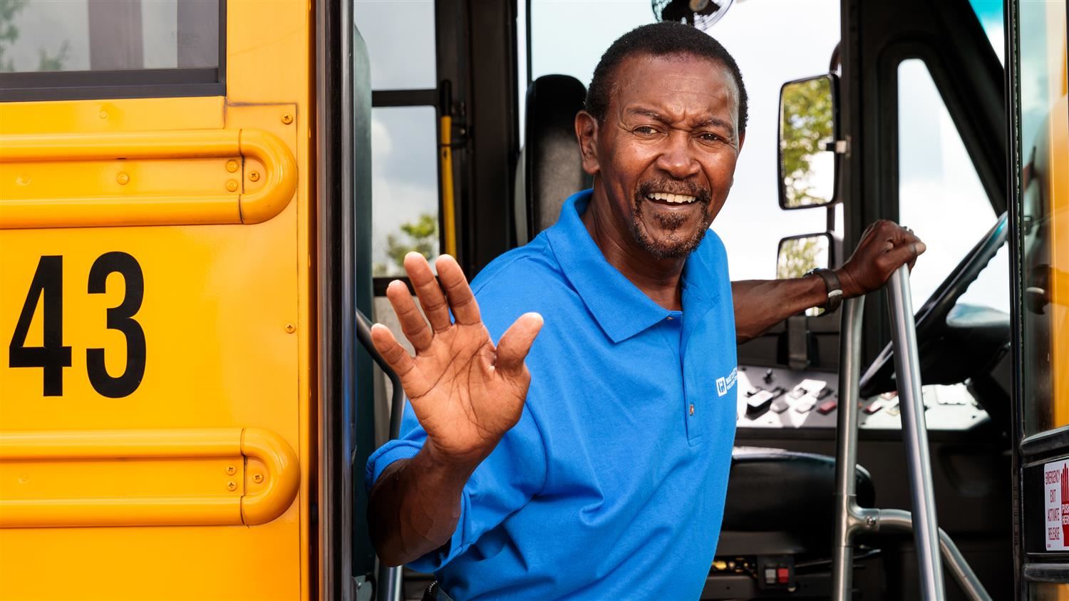 Male driver waving from school bus door.